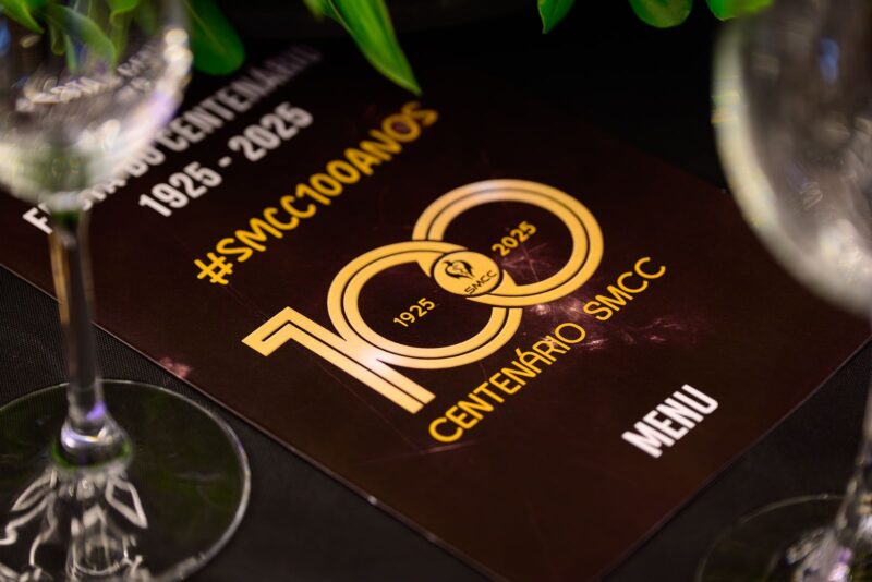Cardápio personalizado com a identidade do centenário sobre a mesa na Festa do Centenário da SMCC